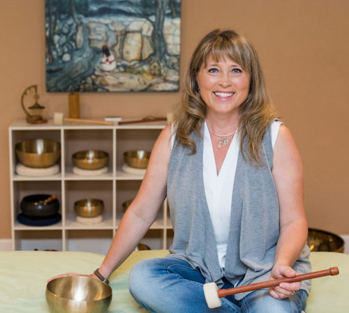 Dr. Brenda Negley sitting with a sound bowl and a set of sound bowls behind her.